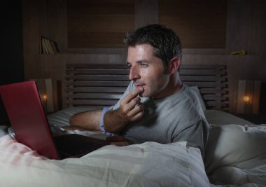 genç çekici ve rahat adam evde ağ yatak gece geç saatlerde dizüstü bilgisayar ya da çalışma zevk internet sosyal medya seyir üzerinde neşeli ve memnun mutlu yazarak üzerinde rahat yalan