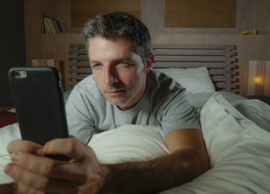yaşam tarzı ev yatak ağ mutlu ve neşeli yalan gece geç onun yatak odasında cep telefonunda internet sosyal medya uygulaması kullanan genç çekici ve rahat adam portresi