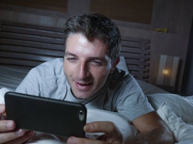 yaşam tarzı ev yatak ağ mutlu ve neşeli gülümseyen üzerinde yalan gece geç onun yatak odasında cep telefonunda internet sosyal medya uygulaması kullanan genç çekici ve rahat adam portresi
