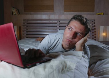 genç çekici yorgun ve mutsuz adam üzgün yalan gece geç vurguladı ve iş stres kavramı içinde boğulmuş ağ yatakta yorgun yatakta dizüstü bilgisayar ile çalışma
