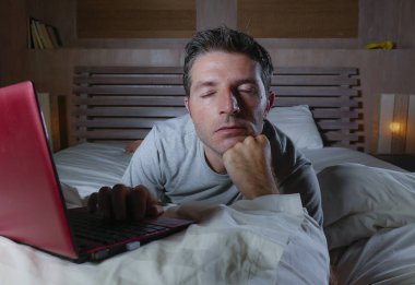 genç çekici yorgun ve mutsuz adam üzgün yalan gece geç vurguladı ve iş stres kavramı içinde boğulmuş ağ yatakta yorgun yatakta dizüstü bilgisayar ile çalışma