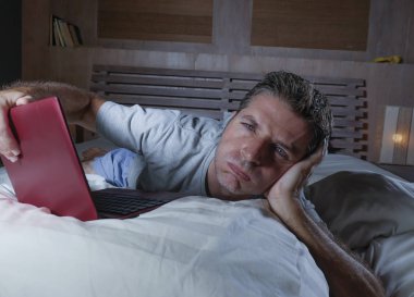 genç çekici yorgun ve mutsuz adam üzgün yalan gece geç vurguladı ve iş stres kavramı içinde boğulmuş ağ yatakta yorgun yatakta dizüstü bilgisayar ile çalışma