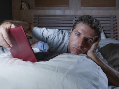 genç çekici yorgun ve mutsuz adam üzgün yalan gece geç vurguladı ve iş stres kavramı içinde boğulmuş ağ yatakta yorgun yatakta dizüstü bilgisayar ile çalışma