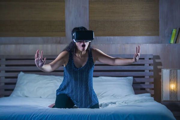 young attractive excited and happy girl wearing VR virtual reality gaming headset playing enjoying amazed the digital 3D experience watching and touching the illusion on bed