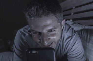 genç yakışıklı ve çekici mutlu adam cep telefonu sosyal medya zevk veya internet bağımlılığı app dating online rahat yatak gülümseyen içinde gece geç ile ağ 