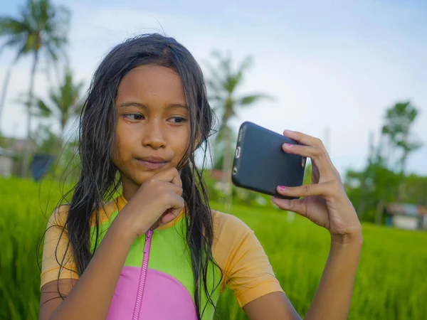 7 or 8 years old sweet and pretty female child outdoors at rice field landscape taking selfie portrait  photo with mobile phone camera enjoying holidays in children and internet technology concept