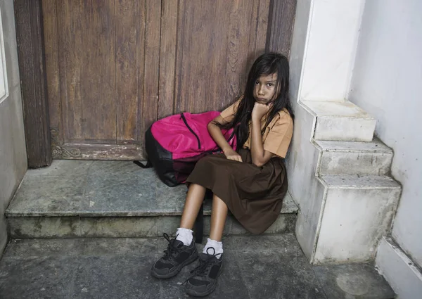 7 oder 8 Jahre Kind in Schuluniform sitzt traurig und deprimiert mit seinem Rucksack auf der Treppe und leidet unter Mobbing- und Missbrauchsproblemen, fühlt sich allein und hilflos — Stockfoto