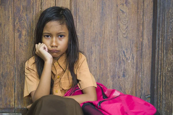 7 oder 8 Jahre Kind in Schuluniform sitzt traurig und deprimiert mit seinem Rucksack auf der Treppe und leidet unter Mobbing- und Missbrauchsproblemen, fühlt sich allein und hilflos — Stockfoto
