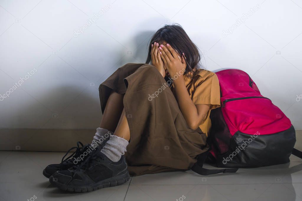 depressed 8 or 9 years old child in school uniform sitting on the floor with her bad crying helpless feeling scared and desperate suffering bullying and abuse 