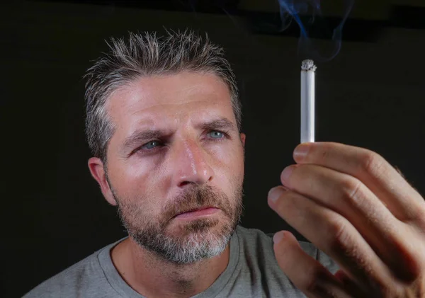 Bonito e pensativo viciado em tabaco homem segurando cigarro pensando tempo para parar de fumar isolado em fundo preto em mau hábito e vício conceito — Fotografia de Stock