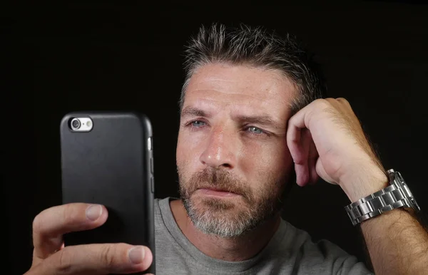 Young attractive and confident white man with blue eyes  using online dating app or internet social media on mobile phone isolated on black background — Stock Photo, Image