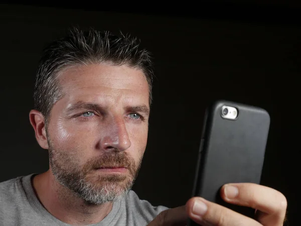 Jovem atraente e confiante homem branco com olhos azuis usando on-line namoro aplicativo ou internet mídia social no telefone celular isolado no fundo preto — Fotografia de Stock