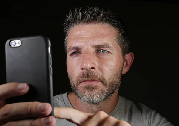 young attractive and confident white man with blue eyes  using online dating app or internet social media on mobile phone isolated on black background