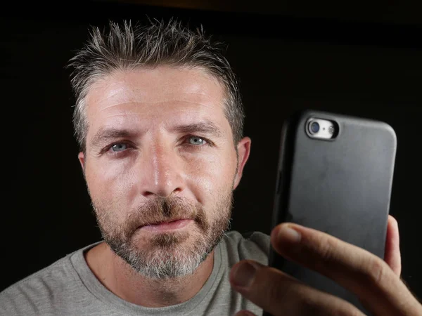 Jovem atraente e confiante homem branco com olhos azuis usando on-line namoro aplicativo ou internet mídia social no telefone celular isolado no fundo preto — Fotografia de Stock