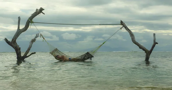 Homme couché détendu et heureux dans l'hamac de mer incroyable mis en place sur troncs d'arbres à la plage de l'île tropicale dans des vacances relaxantes escapade de voyage et destination touristique — Photo