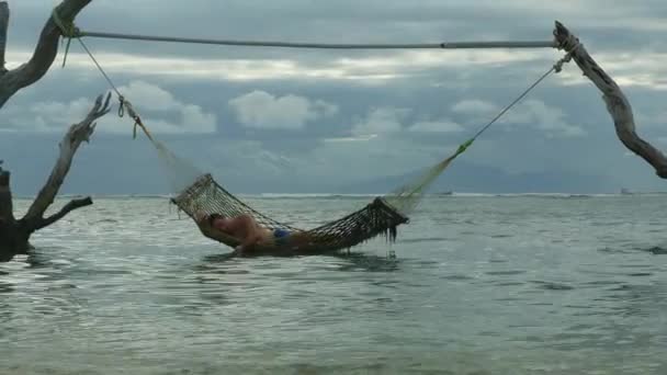 男子躺在放松和快乐的睡眠午睡在海上吊床惊人设置在树干上的热带岛屿海滩在轻松的假期旅行出游和旅游目的地的概念 — 图库视频影像