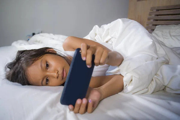 Feliz y hermoso niño de 7 años de edad que se divierten jugando juego de Internet con el teléfono móvil acostado en la cama alegre y emocionado en la niña y el concepto de tecnología — Foto de Stock