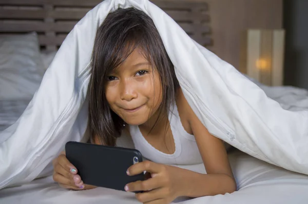 Feliz y hermoso niño de 7 años de edad que se divierten jugando juego de Internet con el teléfono móvil acostado en la cama alegre y emocionado en concepto de tecnología para niños y domésticos — Foto de Stock