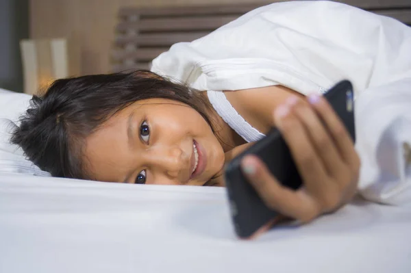 Feliz y hermoso niño de 7 años de edad que se divierten jugando juego de Internet con el teléfono móvil acostado en la cama alegre y emocionado en concepto de tecnología para niños y domésticos — Foto de Stock