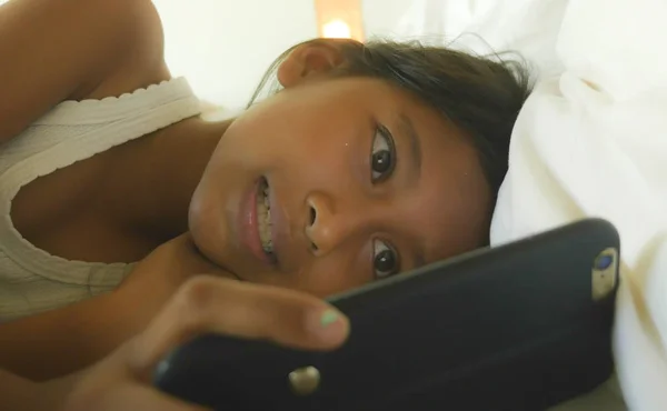 Životní styl portrét sladká holčička, šťastná a krásná mladá dívka baví hrát hru Internetu s mobilním telefonem, ležící na posteli, veselá a vzrušený — Stock fotografie