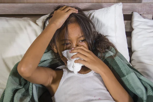 Estilo de vida retrato en casa de una joven hermosa y dulce niña de 8 años sosteniendo papel tisú estornudando su nariz acostada enferma en la cama con gripe o virus del resfriado — Foto de Stock