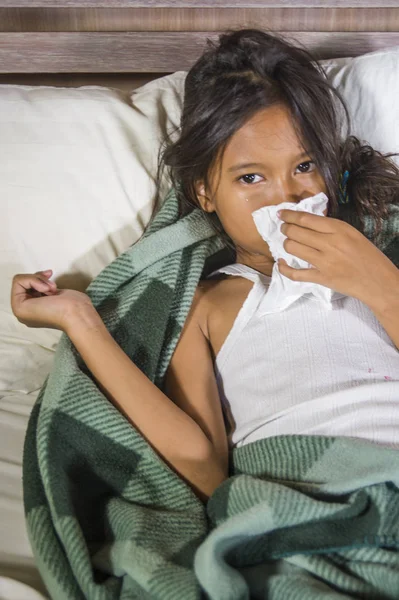 Estilo de vida retrato en casa de una joven hermosa y dulce niña de 8 años sosteniendo papel tisú estornudando su nariz acostada enferma en la cama con gripe o virus del resfriado — Foto de Stock