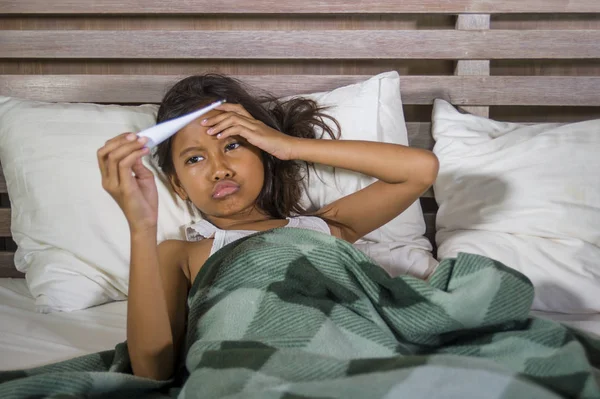 Estilo de vida retrato en casa de una joven hermosa y dulce niña de 8 años sosteniendo el termómetro acostada enferma en la cama con gripe o virus del resfriado sintiéndose triste e incómoda — Foto de Stock