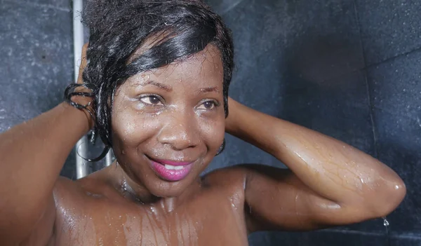 Estilo de vida doméstico retrato de joven feliz y hermoso negro afro mujer americana sonriendo feliz tomando una ducha en casa baño lavándose el pelo con champú — Foto de Stock