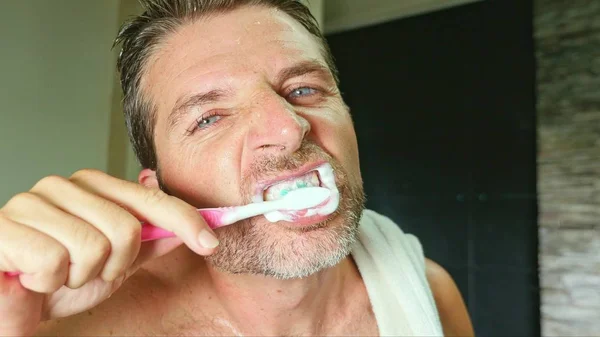 Lifestyle πορτραίτο νεαρού όμορφος και ελκυστικός με μπλε μάτια στο σπίτι μπάνιο με πετσέτα στον ώμο πλύσιμο τα δόντια με οδοντόβουρτσα στη στοματική υγιεινή — Φωτογραφία Αρχείου