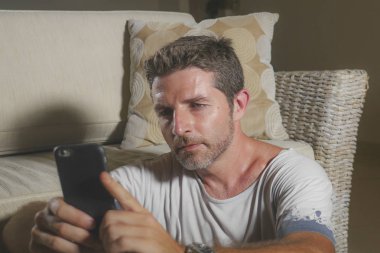 oturma odası katında oturan genç çekici ve yakışıklı adam odaklı ve hareket eden ağ veya online rahat uzanan telefon kullanarak konsantre