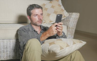 oturma odası katında oturan genç çekici ve yakışıklı adam odaklı ve hareket eden ağ veya online rahat uzanan telefon kullanarak konsantre