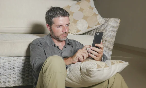 Joven atractivo y guapo hombre sentado en el piso de la sala de estar enfocado y concentrado utilizando redes de telefonía móvil o citas en línea relajado — Foto de Stock