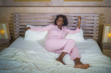 mutlu ve güzel siyah Afrikalı-Amerikalı kadın rahat ve eğlenceli neşeli ve olumlu, iyimser ve taze sabah uyanma gülümseyen yatakta yatarken pijama