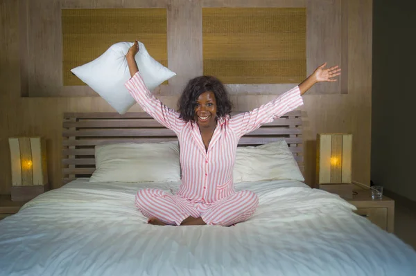Молодая счастливая и красивая черная афро американка в пижаме лежала расслабленной и игривой на кровати улыбаясь веселый и позитивный просыпаясь утром оптимистичный и свежий — стоковое фото