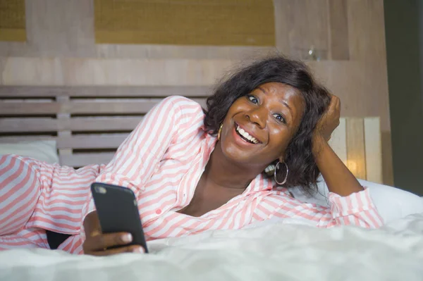 Jovem feliz e bonita negra afro-americana em pijama deitado sorridente relaxado alegre e fresco usando internet rede de telefonia móvel ou on-line namoro — Fotografia de Stock