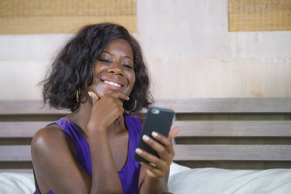 Hermosa y feliz negro afroamericana mujer sentada en la cama usando internet teléfono móvil sonriendo alegre y relajado networking en línea de negocios o redes sociales — Foto de Stock