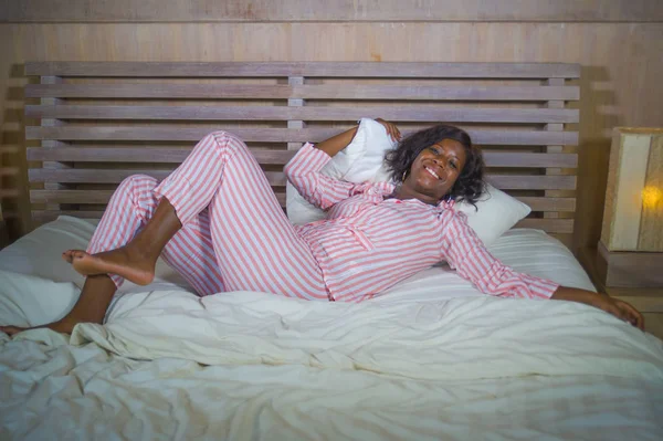 Молодая счастливая и красивая черная афроамериканка в пижаме лежала расслабленной и игривой на кровати улыбаясь веселый и позитивный просыпаясь утром оптимистичный и свежий — стоковое фото