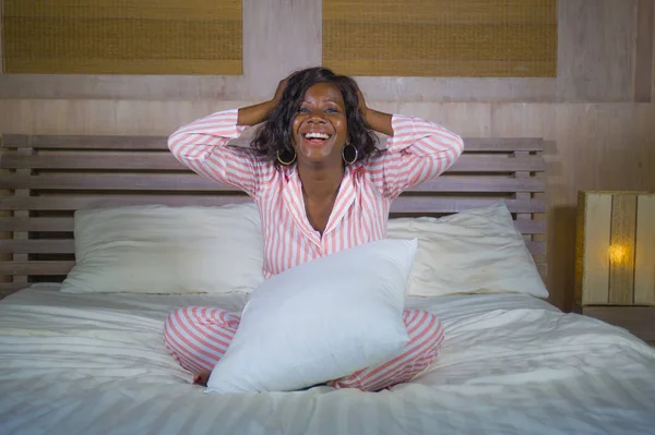 幸せで、美しい黒いアフリカ系アメリカ人の若い女性パジャマ リラックスして遊び心が明るくて前向きな楽観的な新鮮な朝の目覚めを笑ってベッドの上で横になっています。 — ストック写真