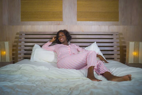 young happy and beautiful black afro American woman in pajamas lying relaxed and playful on bed smiling cheerful and positive waking up in the morning optimistic and fresh