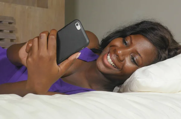 beautiful and happy black Afro American woman lying relaxed on bed using internet mobile phone smiling cheerful networking social media business or online dating