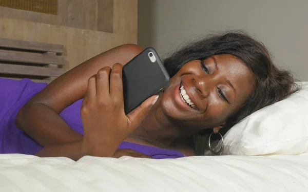 Beautiful and happy black Afro American woman lying relaxed on bed using internet mobile phone smiling cheerful networking social media business or online dating — Stock Photo, Image