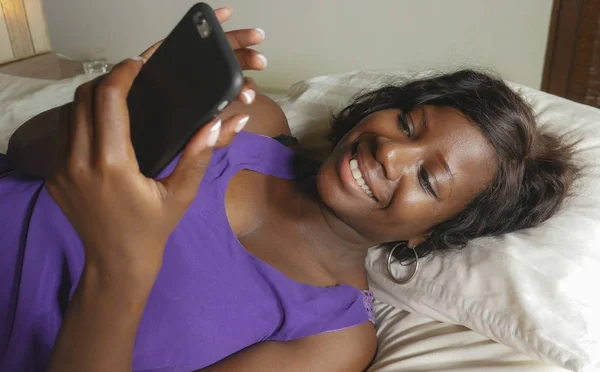 Hermosa y feliz negro Afro mujer americana tumbado relajado en la cama usando internet teléfono móvil sonriendo alegre creación de redes sociales de negocios o en línea citas — Foto de Stock