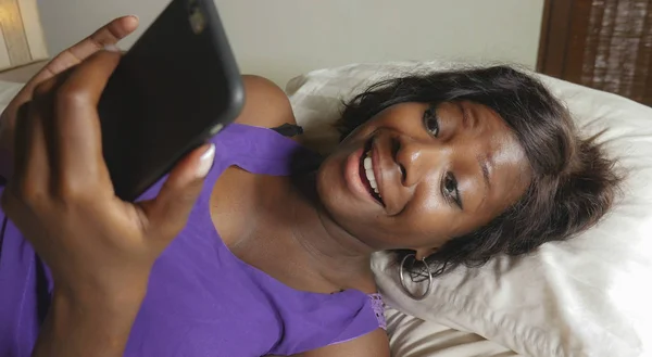 Hermosa y feliz negro Afro mujer americana tumbado relajado en la cama usando internet teléfono móvil sonriendo alegre creación de redes sociales de negocios o en línea citas — Foto de Stock