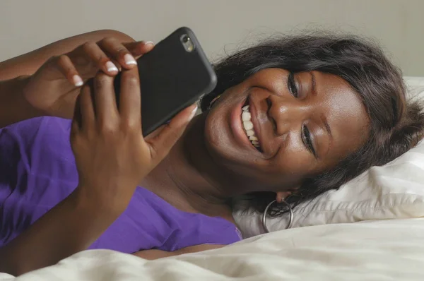 Hermosa y feliz negro mujer afroamericana tumbado relajado en la cama usando internet teléfono móvil sonriendo alegre creación de redes sociales de negocios o en línea citas —  Fotos de Stock