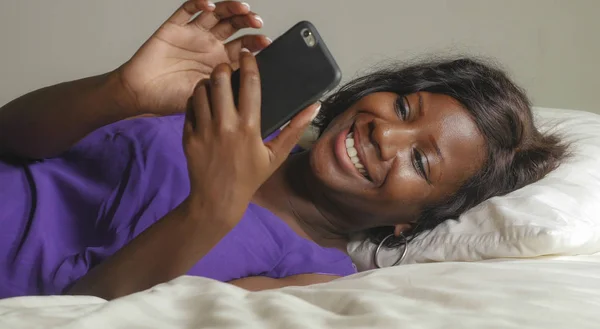 Beautiful and happy black African American woman lying relaxed on bed using internet mobile phone smiling cheerful networking social media business or online dating — Stock Photo, Image