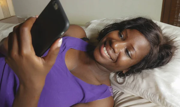 Beautiful and happy black African American woman lying relaxed on bed using internet mobile phone smiling cheerful networking social media business or online dating — Stock Photo, Image