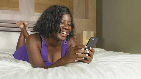 Szép és boldog fekete Afro-amerikai nő, fekvő nyugodt ágyon, mosolygó, vidám hálózati társadalmi média üzleti vagy online társkereső internetes mobiltelefon használata — Stock Fotó