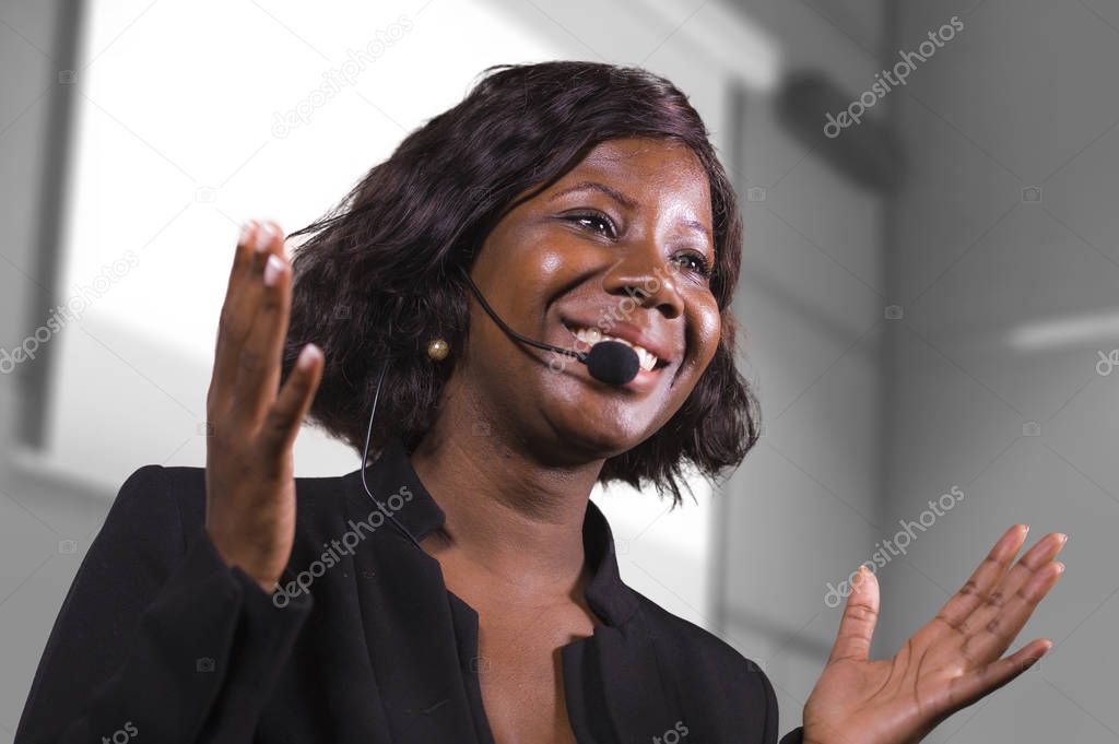 young attractive and confident black African American business woman with headset speaking in auditorium at corporate training event or seminar giving motivation conference