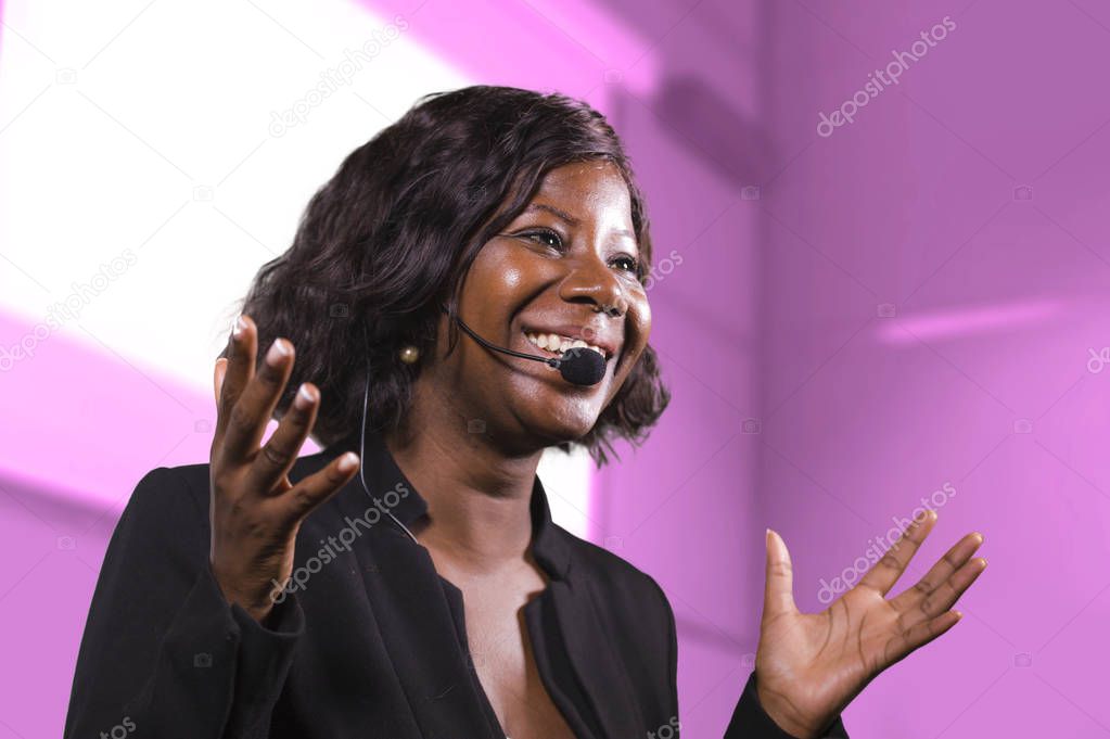 successful black afro American business woman with headset speaking in auditorium at corporate training event or seminar giving motivation and success coaching