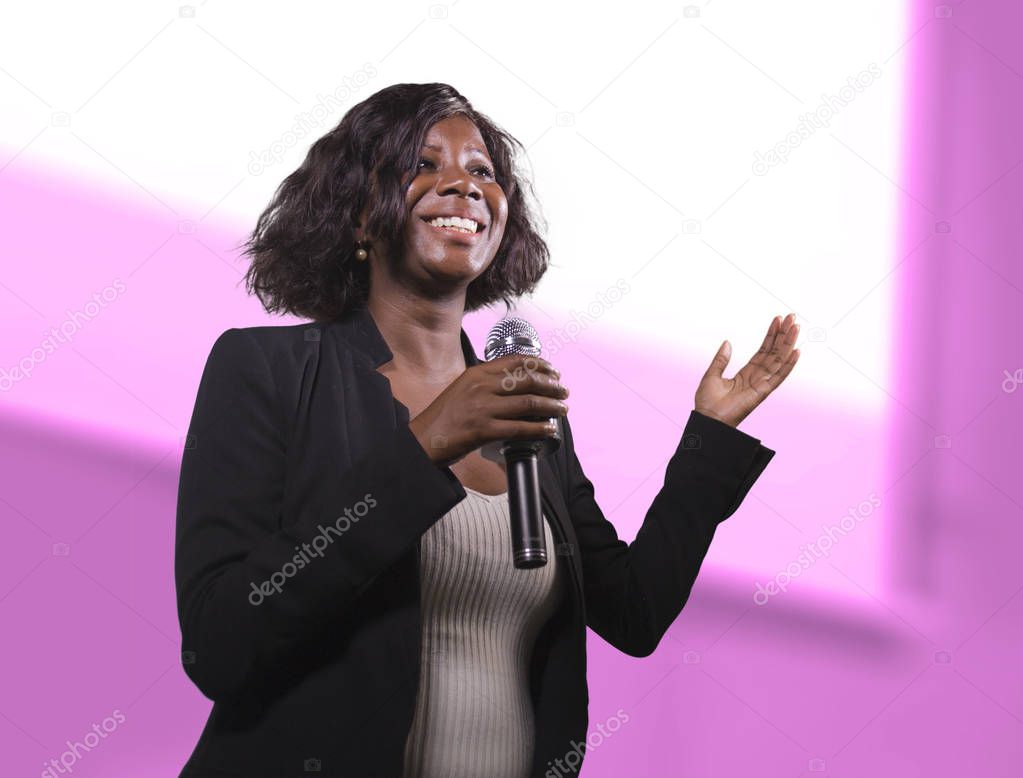  confident black afro American business woman with microphone speaking in auditorium at corporate event or seminar giving motivation and success coaching